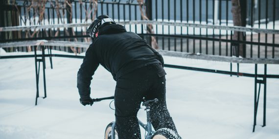 A man in black jacket riding on black bmx bike on snow