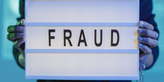 A person with handcuffs holding a sign that says fraud