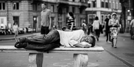 man sleeping on bench in the middle of the street