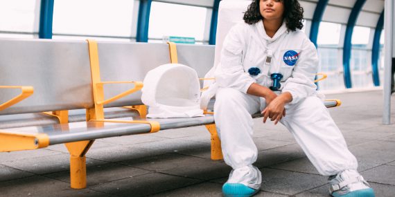 Young woman in space suit sitting on a public waiting chairs