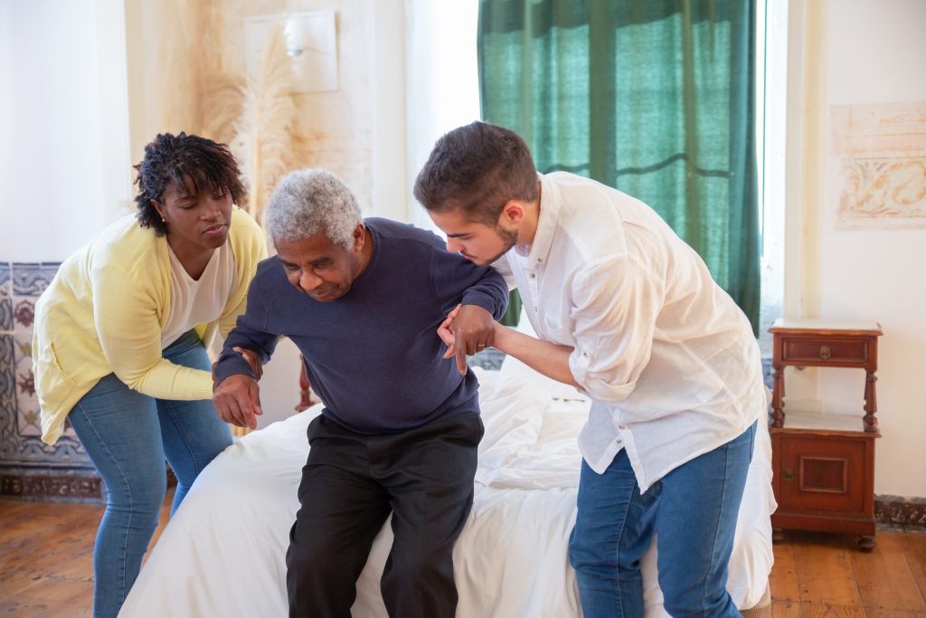 A man and a woman assisting an elderly man in standing