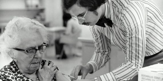 grayscale photography of man holding syringe injecting on woman left arm