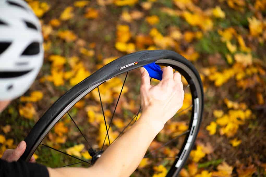 Biker fixing a flat bike tire in a park with autumn leaves. Close-up shot.
