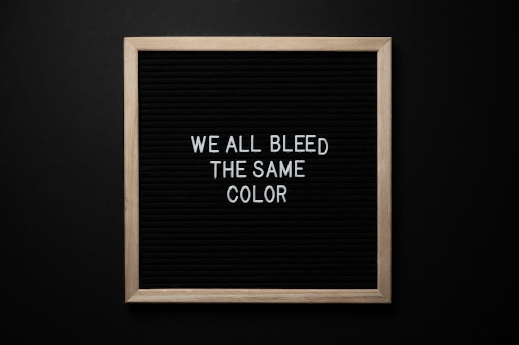 Top view of black signboard with phrase We All Bleed Same Color on surface on black background