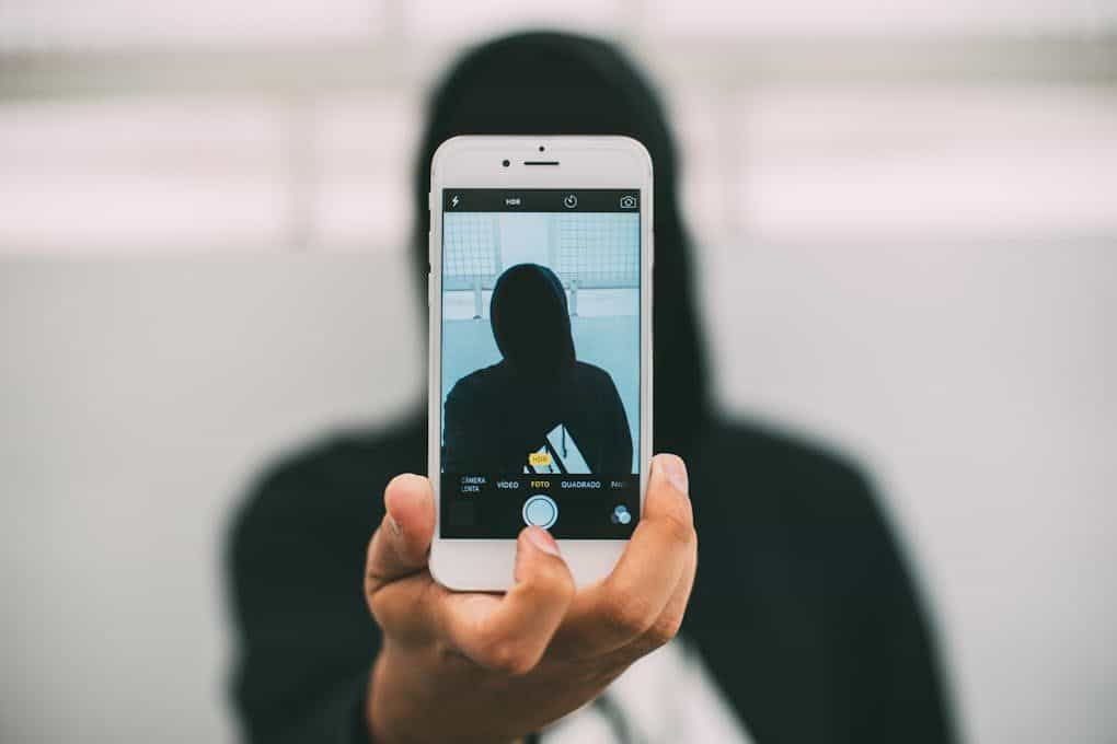 A person in a hoodie takes a mysterious selfie with a smartphone.