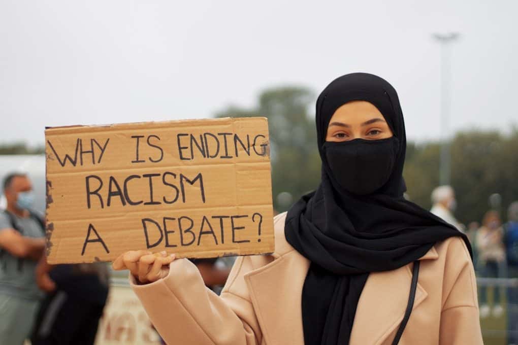 woman in black hijab holding brown wooden welcome to the beach signage